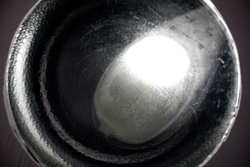 Dark, metallic bowl with a bright, oval-shaped reflection in the center, revealing a fingerprint pattern.