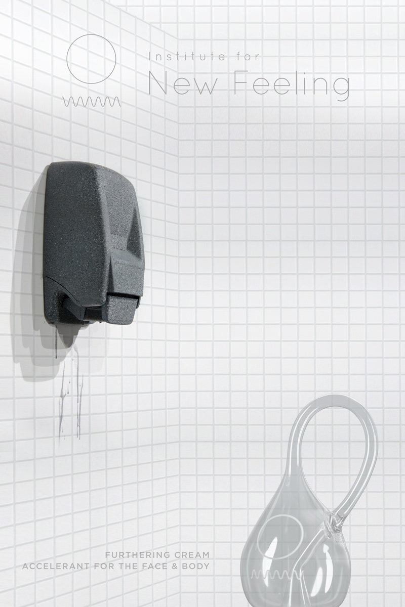 Grey soap dispenser on white tiled wall, dripping liquid. Clear glass loop and text "Institute for New Feeling" on right.