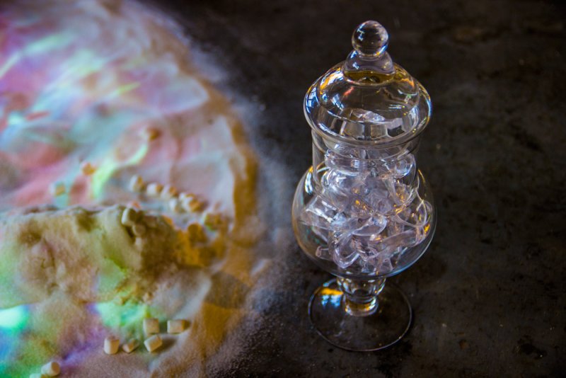Glass jar filled with clear plastic shards next to a pile of white powder with colorful light projections.