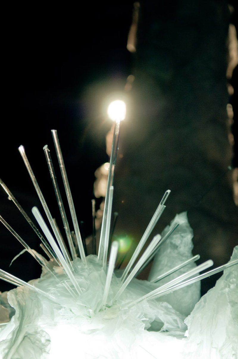 A sculpture of clear rods radiating from a crumpled white base, illuminated by a bright light against a dark background.