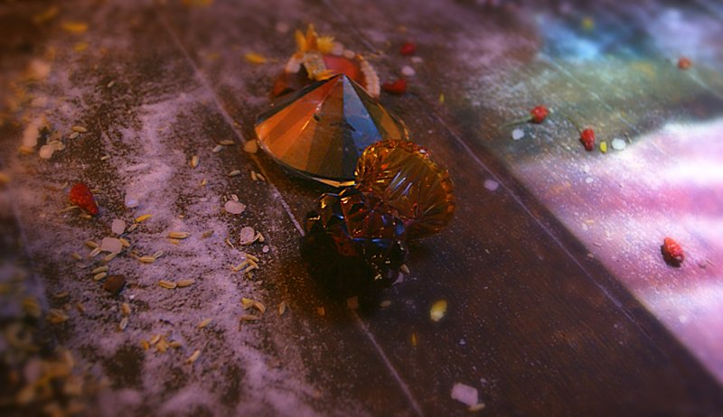 A dark wooden surface covered in white powder, rice, and red berries, featuring two faceted glass objects.