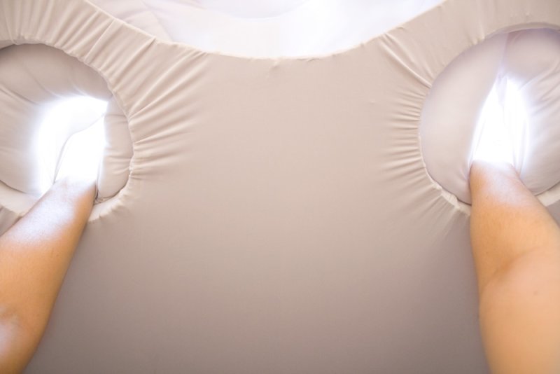 Two arms reach into a light beige, ruffled fabric structure, with bright white light emanating from two openings.