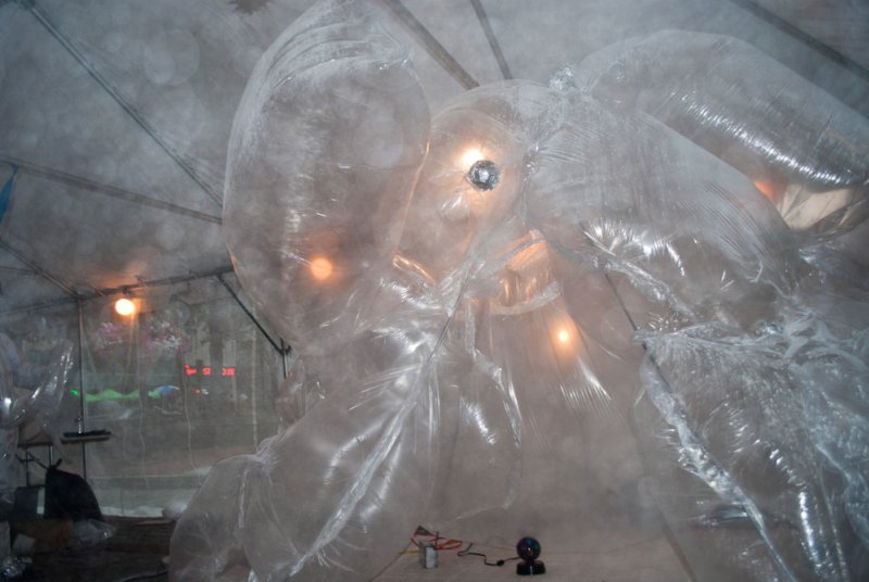 Inflatable clear plastic sculpture with internal lights glowing orange, filling a tent-like space.