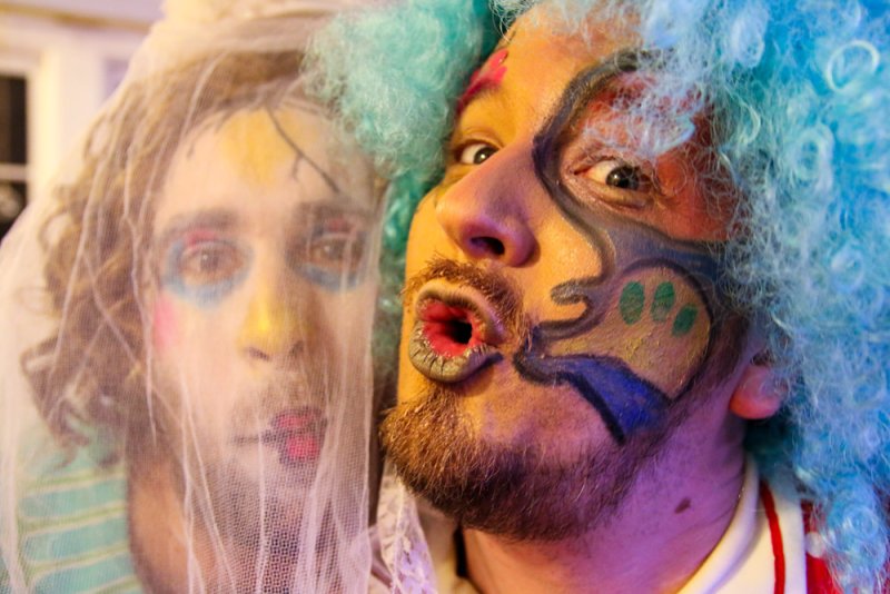 Two self-portraits: one with a white veil, the other with a blue wig and colorful face paint, mouth open.