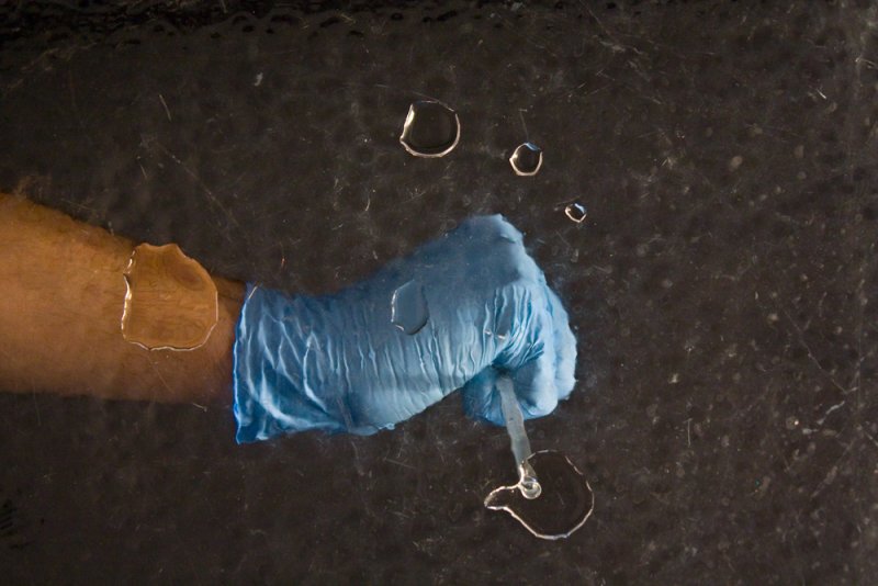 Arm with blue glove and pipette, creating water bubbles on a dark, wet surface.