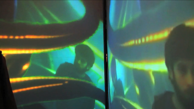 Two screens show a man's face and shoulders, overlaid with glowing green and orange abstract shapes.