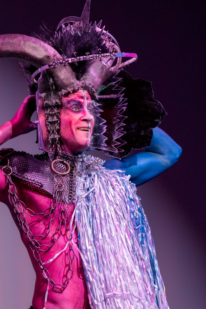 Darrell Thorne in drag, with a pink torso, blue arm, elaborate headdress, and a shimmering silver fringe garment.
