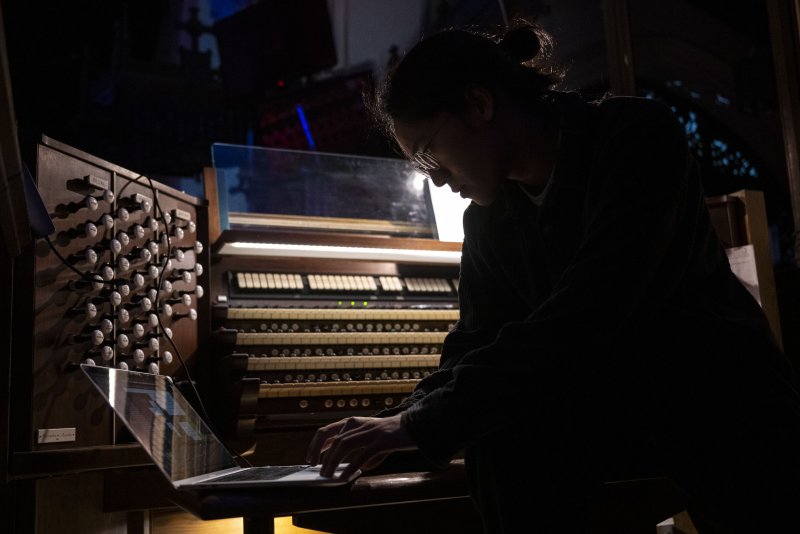Scott N Andrew's "Vox Humana" (2024) shows a person in profile, silhouetted, playing an organ and looking at a laptop.