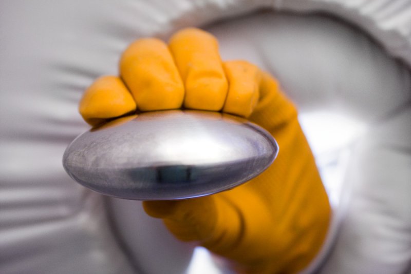 A person in a white hazmat suit and orange gloves holds a shiny, metallic, disc-shaped object.