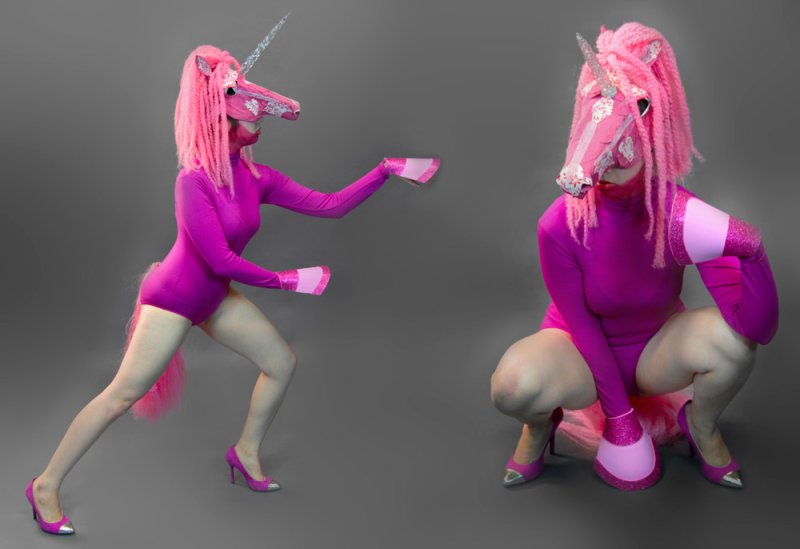 Two figures in pink unicorn masks and bodysuits, one lunging left, the other crouching right, against a gray background.