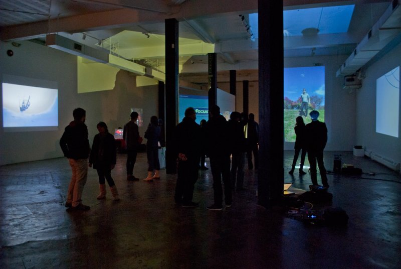 Dark gallery with silhouetted figures viewing projected artworks, one showing a person in a field, another a swirling form.