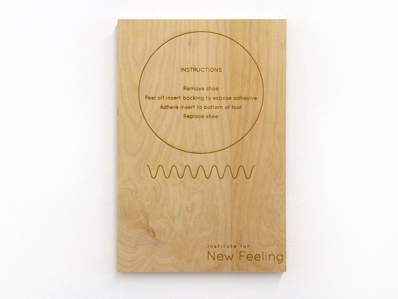 Light wood panel with engraved instructions, a circular outline, a wavy line, and "Institute for New Feeling" text.