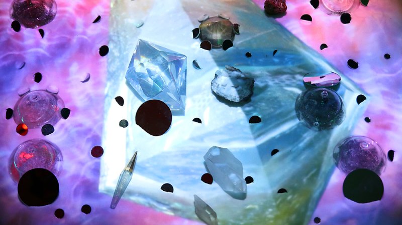 Abstract image with a purple and blue background, featuring various crystals, shiny objects, and black circular shapes.