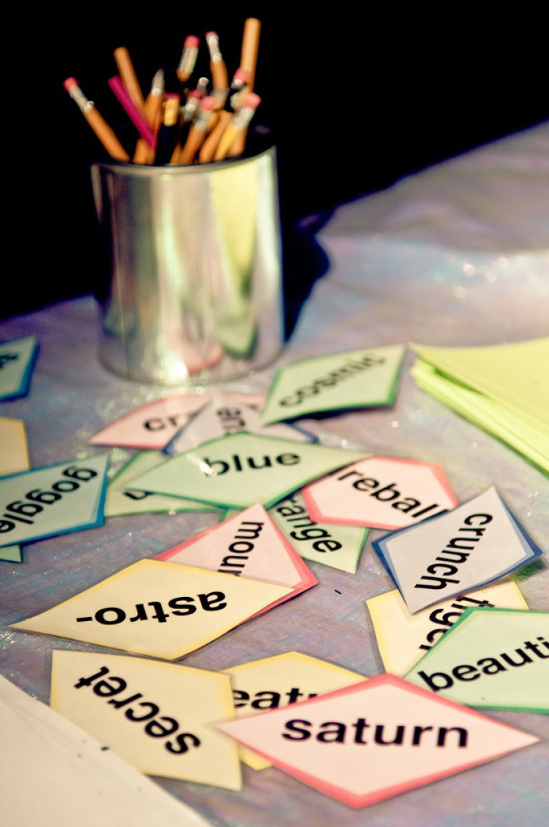 Colorful word cutouts like "astro," "saturn," and "cosmic" scattered on a table with a can of pencils.