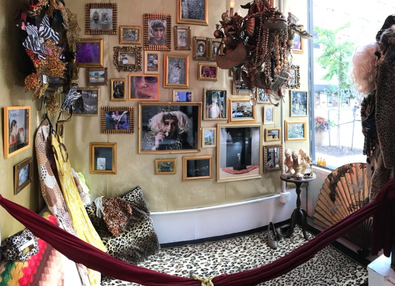 Eclectic gallery wall with many framed photos, a large beaded chandelier, leopard print carpet, and a red hammock.