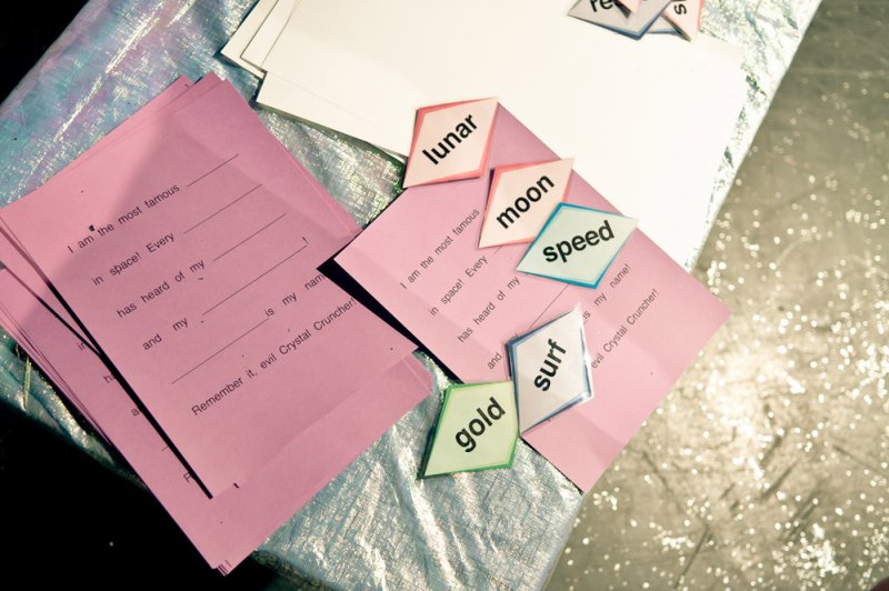 Pink fill-in-the-blank sheets and diamond-shaped word tiles reading "lunar," "moon," "speed," "surf," and "gold.