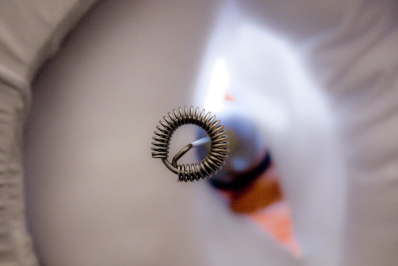 Close-up of a metal whisk coil against a blurry background with a blue object and orange triangle.
