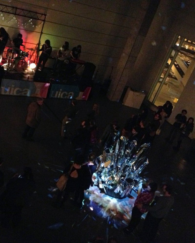 Dark, high-angle view of a band on a stage with red lighting and a large, faceted crystal sculpture reflecting light.