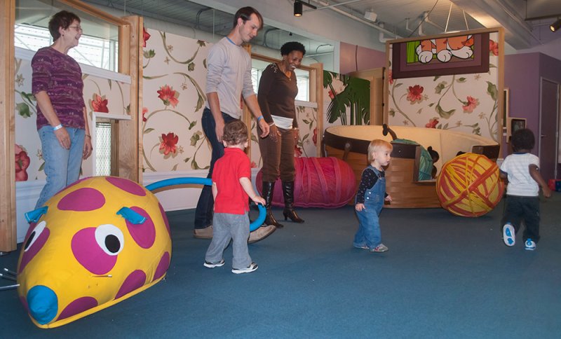 Adults and toddlers in a brightly colored play space with large, soft, abstract animal shapes.